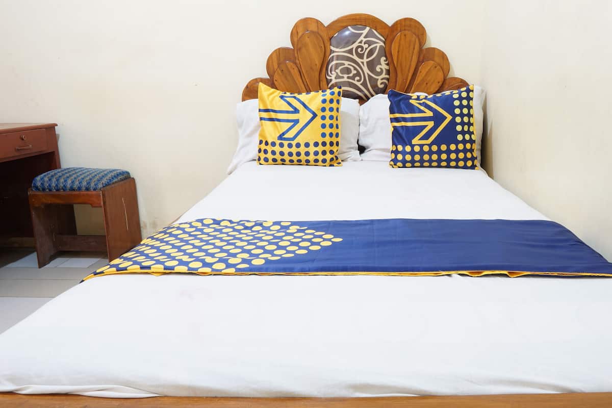 Una cama con cabecera de madera, ropa de cama blanca y almohadas con estampado azul y amarillo.