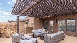 Eine Außenpatio mit Korbmöbeln, einem mit Lichterketten versehenen Pergola, Steinmauern und großen Fenstern.