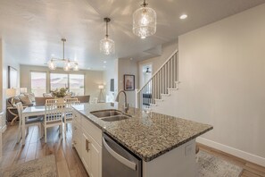 Modern kitchen with central island, stainless steel sink, and dishwasher, adjacent to a dining area with a table and chairs.