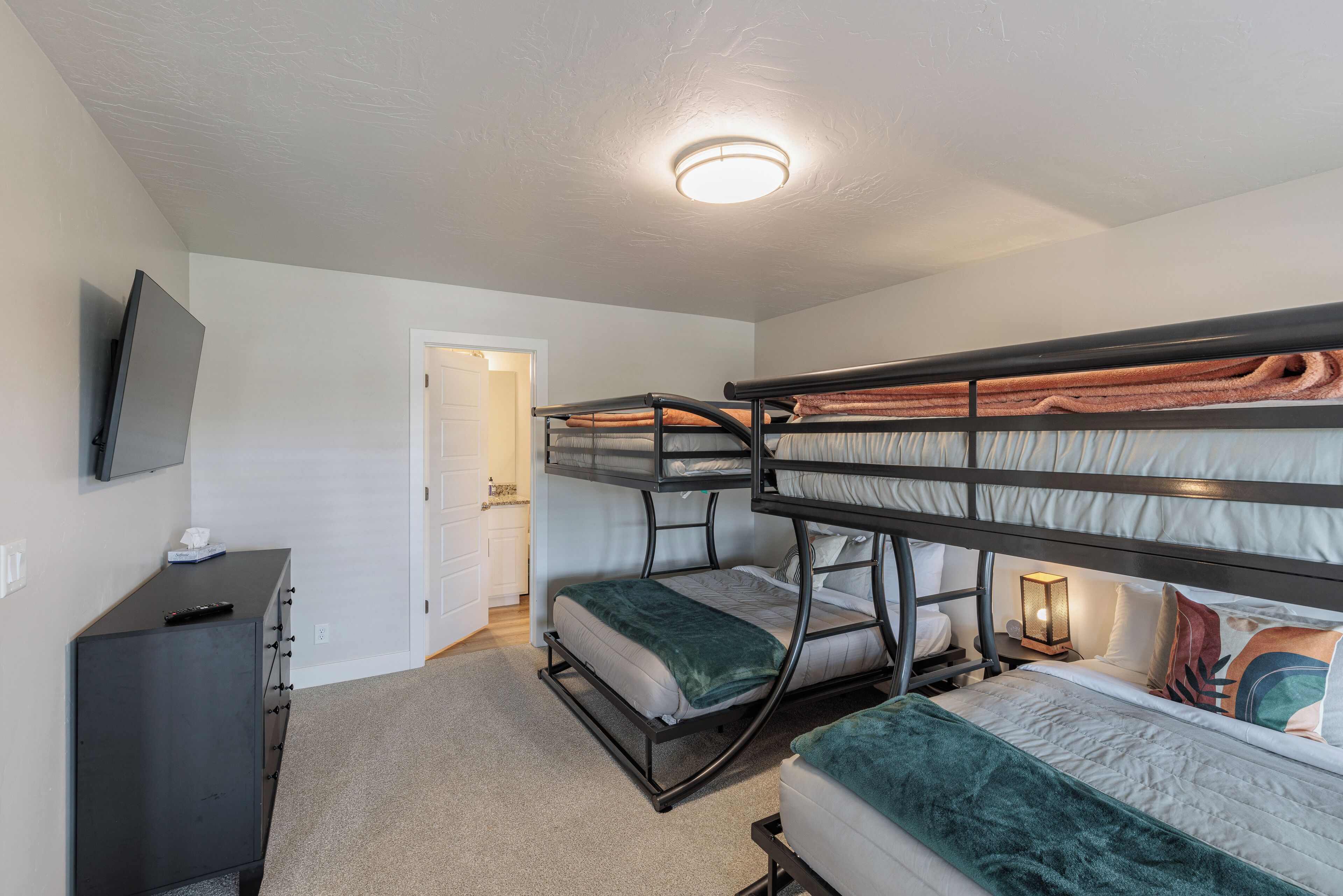 A bunk bed room with a television on a dresser, a door, and a ceiling light.