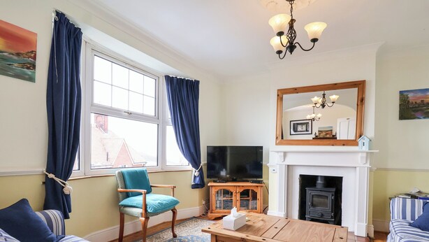 A living room with a sofa, a chair, a wooden coffee table, a television, a fireplace, and a large window with curtains.