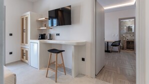 A modern kitchen with a built-in TV, wooden cabinets, and a bar stool. - Adama's Suites Naxos (Naxos)