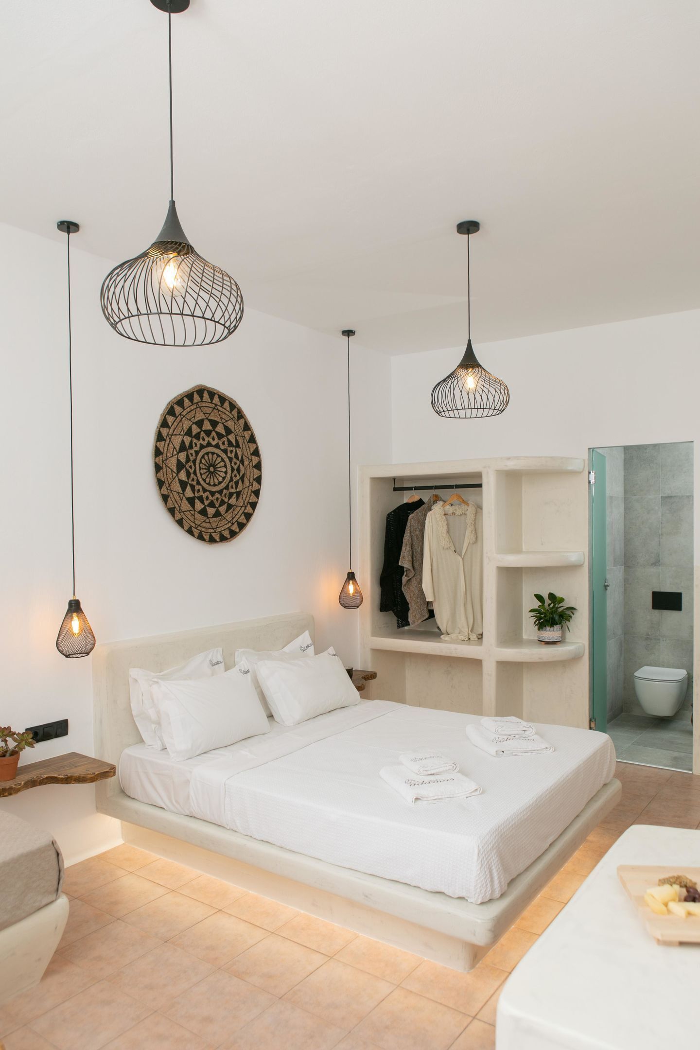 Une chambre moderne avec un lit blanc, des luminaires suspendus, une assiette décorative fixée au mur, un placard intégré et un espace douche.