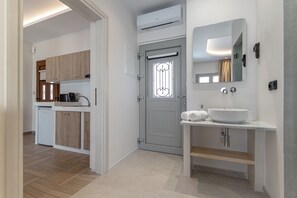 A modern bathroom with a white sink, a large mirror, and a door with a decorative glass panel. - Adama's Suites Naxos (Naxos)