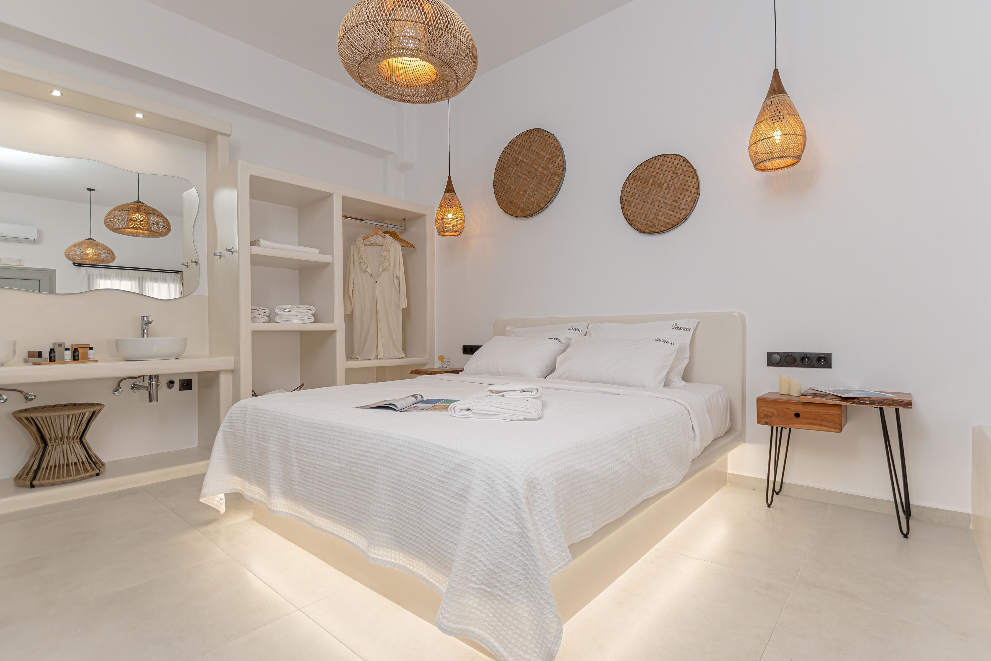 A modern bedroom with a large bed, bedside tables, a wardrobe, and a bathroom with a sink and mirror.