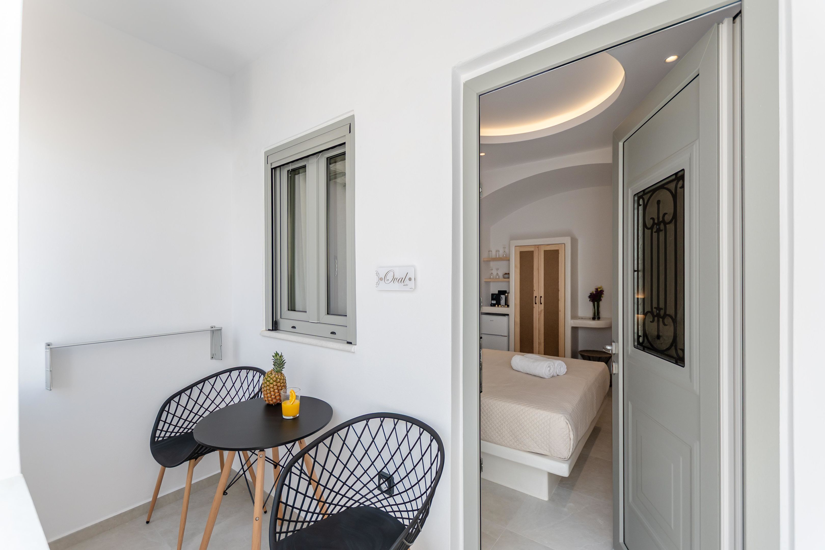 A compact room with a bed, a small table with chairs, a window, and a door leading to another room.