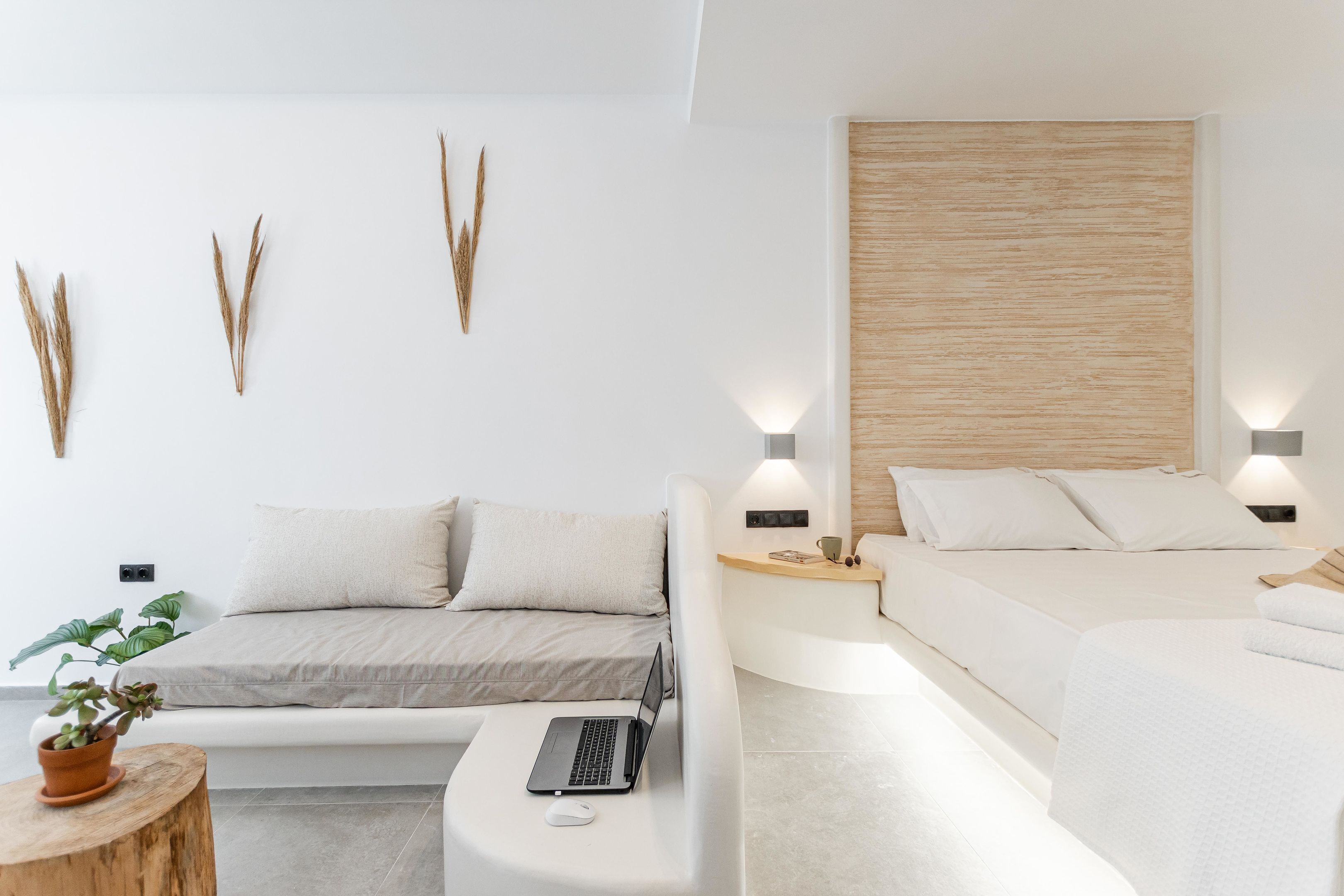 A modern bedroom with a sofa bed, a desk with a laptop, and a wooden headboard.