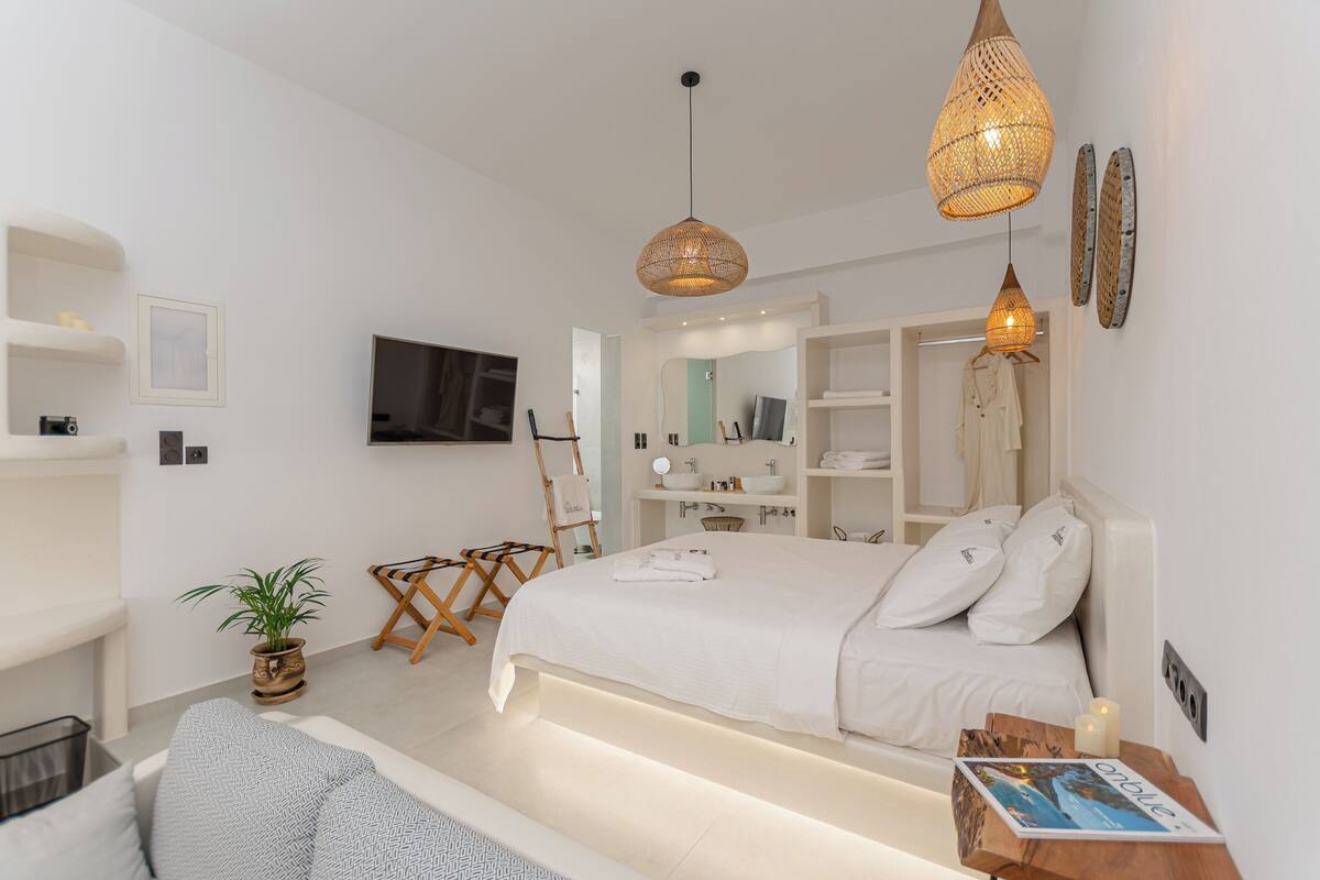 A modern bedroom with a large bed, bedside tables, a TV, and a bathroom with a mirror and sink.