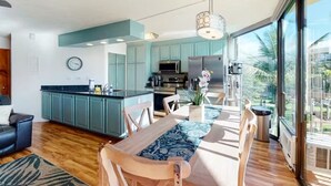 Eine moderne Küche mit türkisblauen Schränken, ein Essbereich mit Holztisch und Stühlen sowie eine große Glasschiebetür, die auf einen Balkon führt.