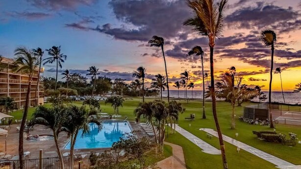 Ein Resort mit Pool, Palmen und Blick auf den Ozean bei Sonnenuntergang.