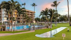 Ein Hotel mit Swimmingpool, umgeben von Palmen, mit Schild, das vor rutschigen Oberflächen bei Nässe warnt.