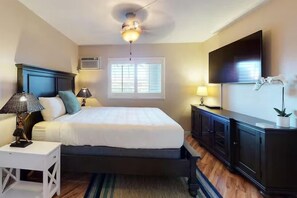 Une chambre à coucher avec un lit, des lampes de chevet, un ventilateur de plafond, une télévision et une fenêtre avec des stores.