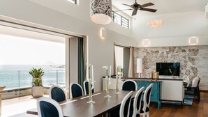 A modern dining area with a view of the sea, a ceiling fan, and a TV mounted on the wall. - Pointe d'Azur by Horizon Holidays (Grand-Baie)