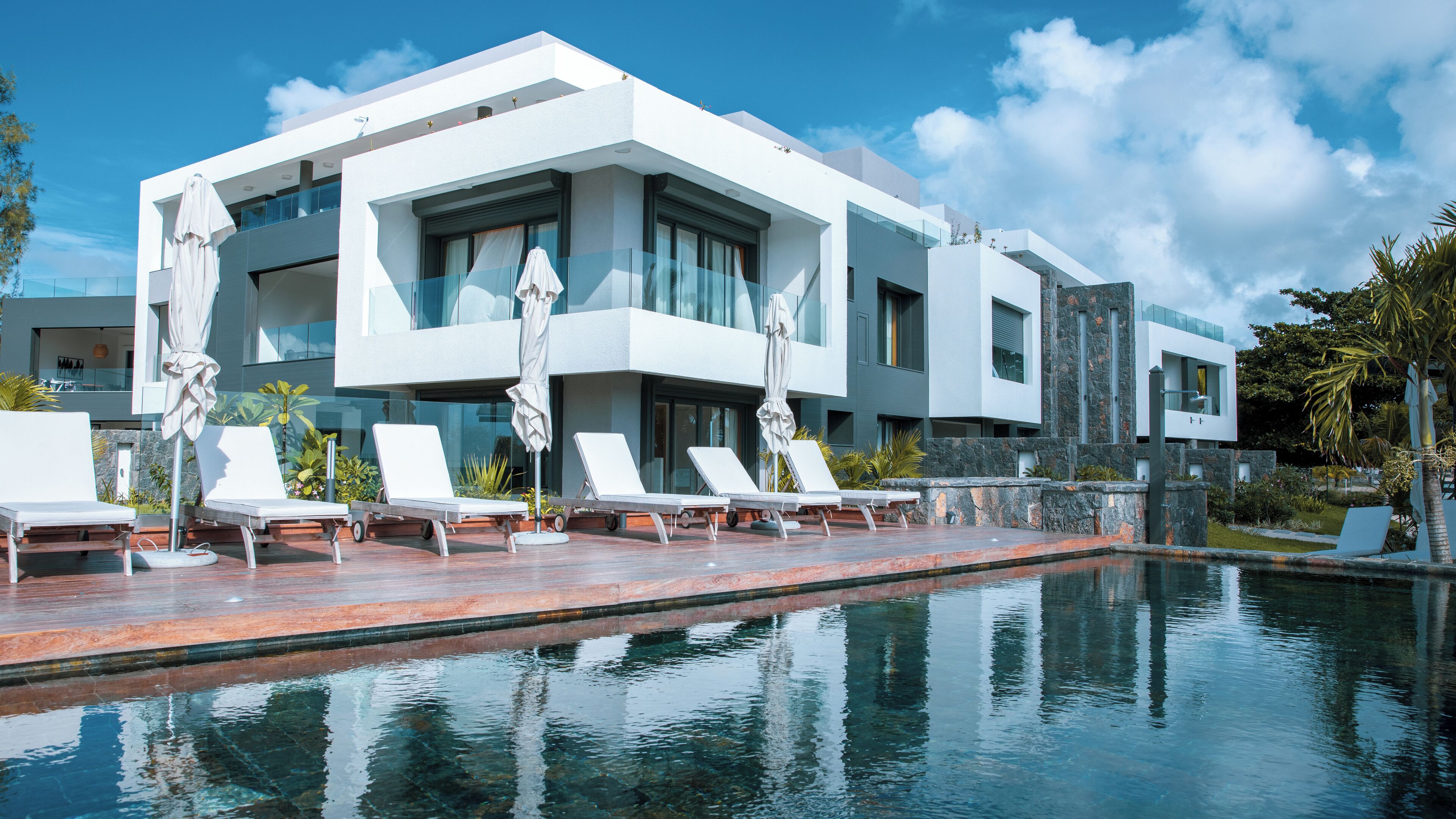 A modern hotel with a pool, white exterior, and multiple lounge chairs.