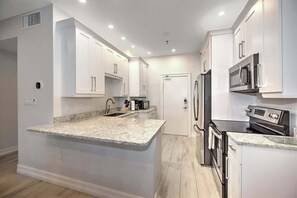 Una cocina moderna con armarios blancos, encimera de granito, electrodomésticos de acero inoxidable e iluminación empotrada en el techo.