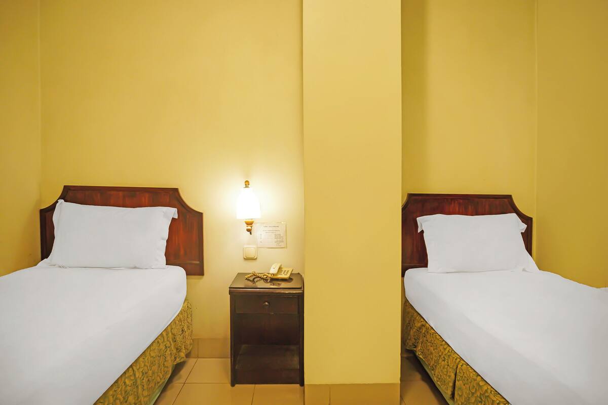 Quarto de hotel com duas camas, uma mesa de cabeceira com abajur e telefone fixado na parede.