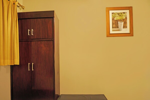 A room with a wooden wardrobe, a framed picture on the wall, and a yellow curtain.
