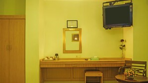 Une pièce comprenant un meuble en bois, une petite table avec un vase, un téléviseur fixé au mur et un tableau encadré au-dessus du meuble.