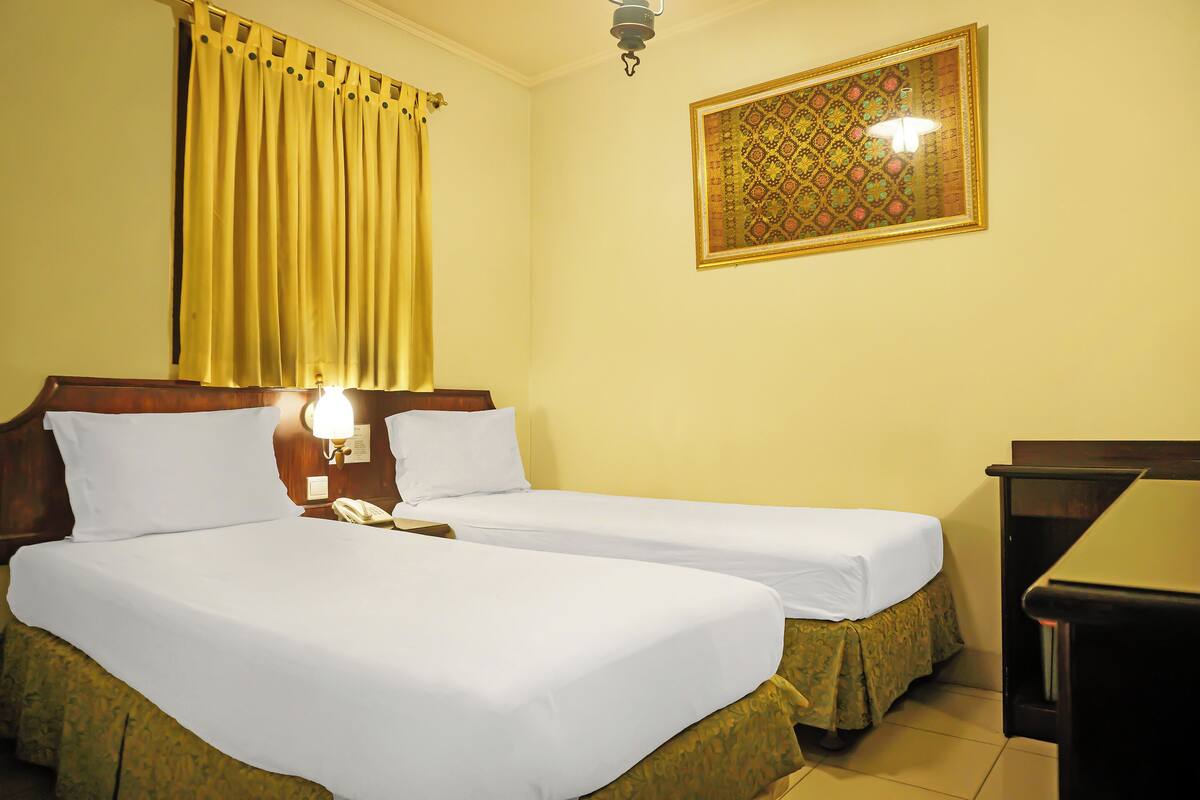 Quarto de hotel com duas camas, mesa de cabeceira com abajur, telefone e um enfeite na parede.