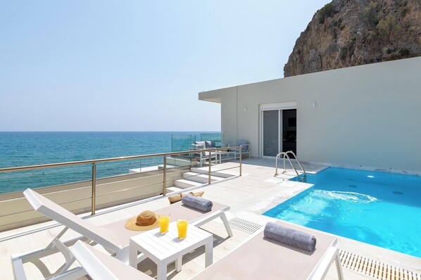 A poolside area with lounge chairs, a table with drinks, and a view of the ocean.