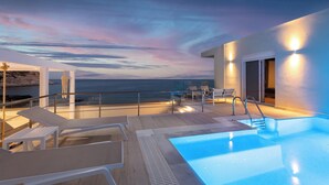 Et tag med swimmingpool, liggestole, jacuzzi og havudsigt i skumringen.
