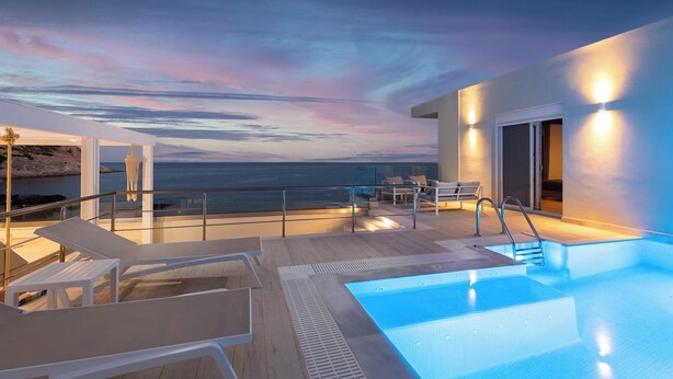 Un espace piscine aménagé sur le toit, avec des chaises longues, un jacuzzi et une vue sur l’océan au crépuscule.