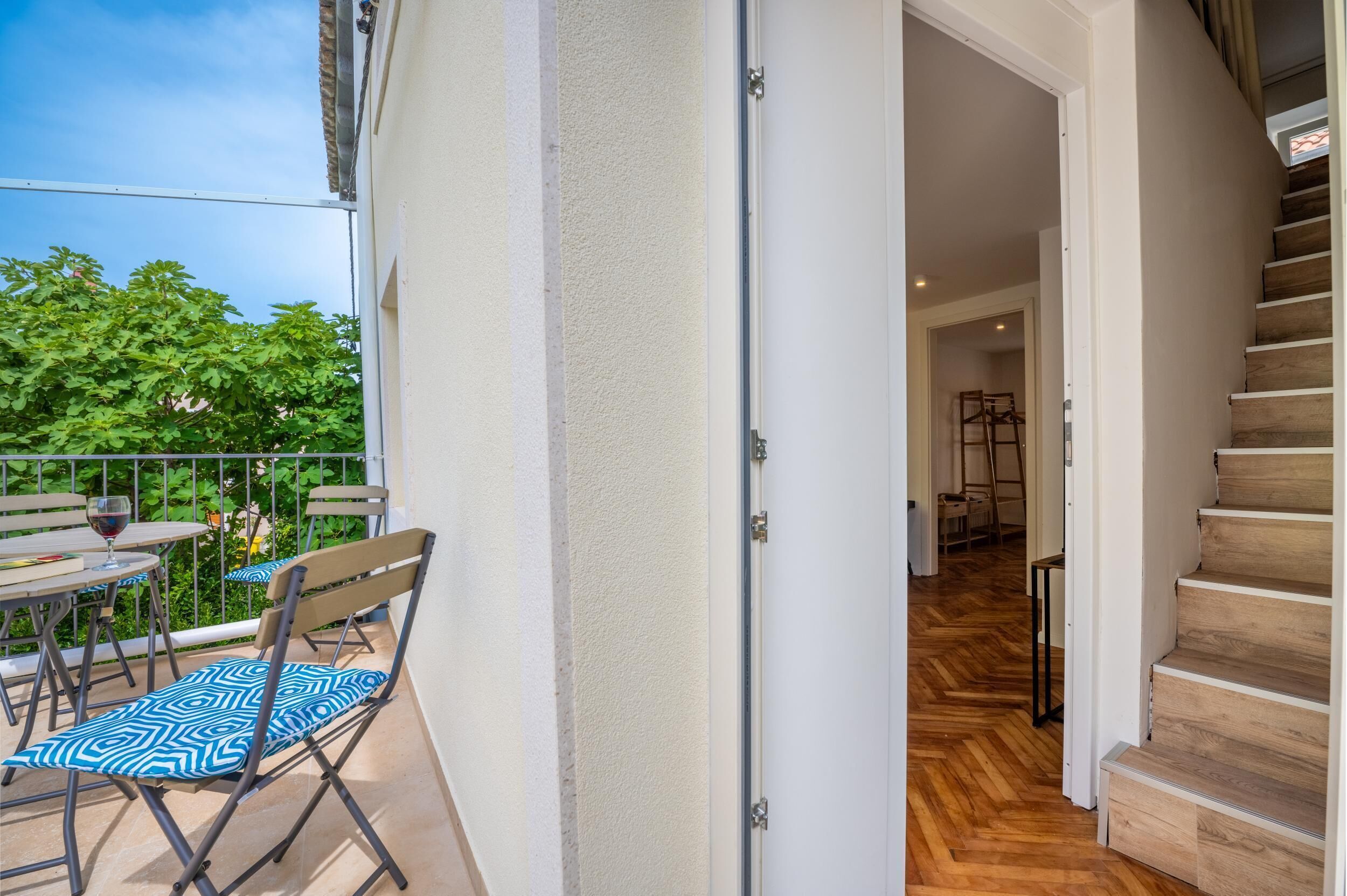 Een open deur die leidt naar een houten trap en een balkon met een tafel en stoelen.