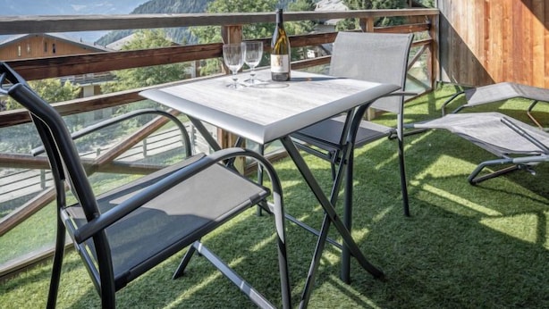 A terrace with a table and chairs, a bottle of wine, and a view of mountains. - Seya 21 by Interhome (Ovronnaz)