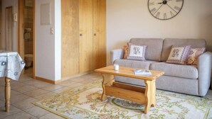 A living room with a sofa, a wooden coffee table, a floral rug, and a wall clock. - Seya 21 by Interhome (Ovronnaz)
