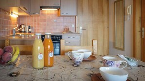 A kitchen with wooden cabinets, a tiled backsplash, and a table set with fruit, bottles, and cups. - Seya 21 by Interhome (Ovronnaz)