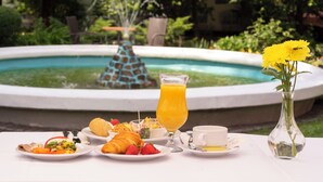 A table with breakfast items, a vase with flowers, and a fountain in the background. - Hotel Hutnik (Stalowa Wola)