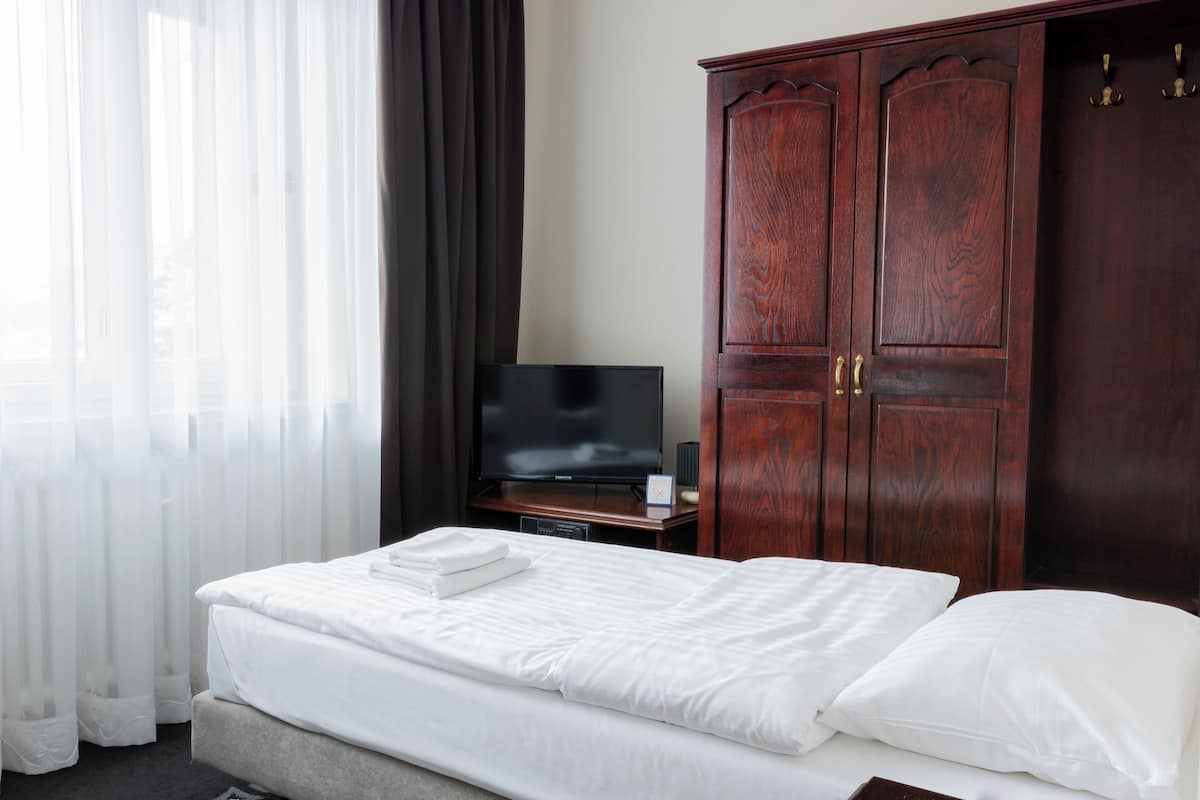 A hotel room with a bed, a television, and a wooden wardrobe.