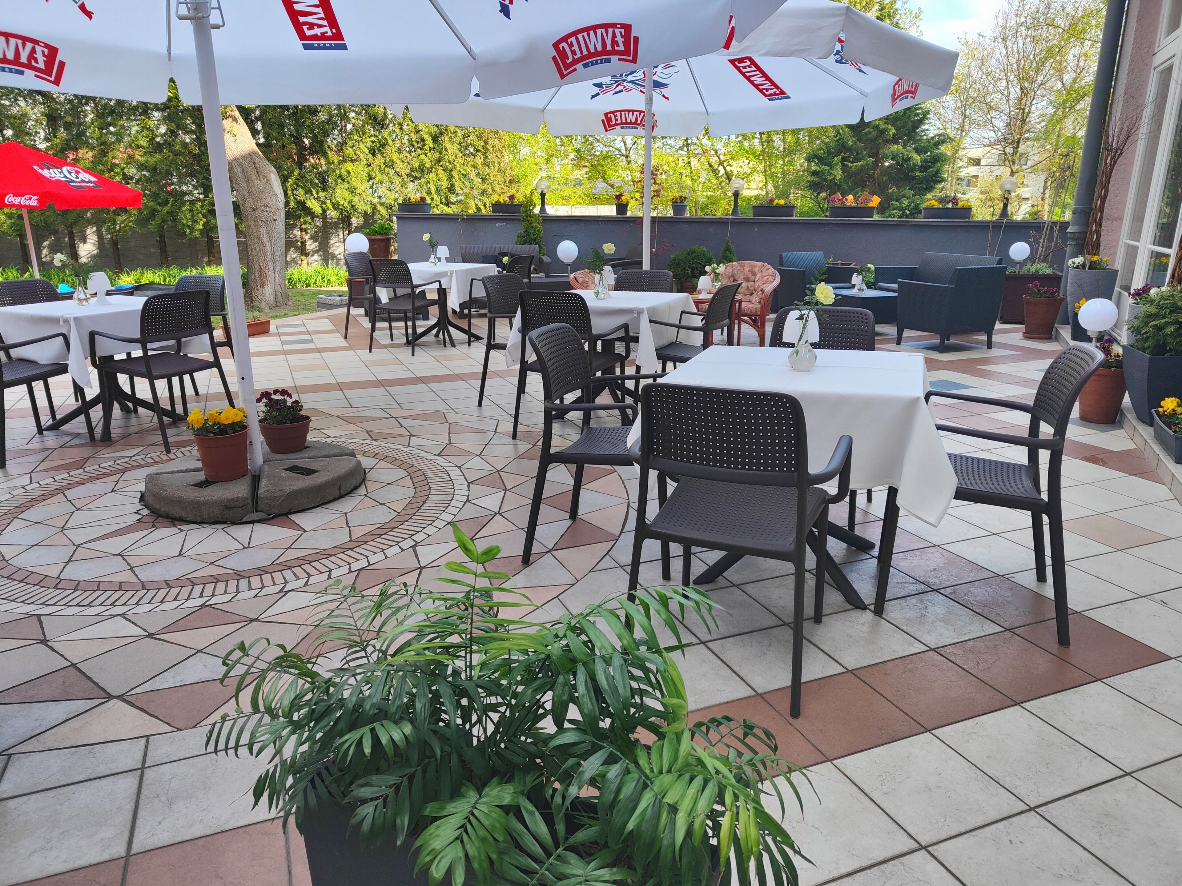 An outdoor patio area with tables and chairs, umbrellas, and potted plants.
