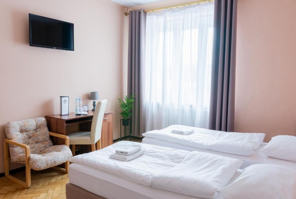 A hotel room with two beds, a desk, a chair, a television, and a window with curtains.