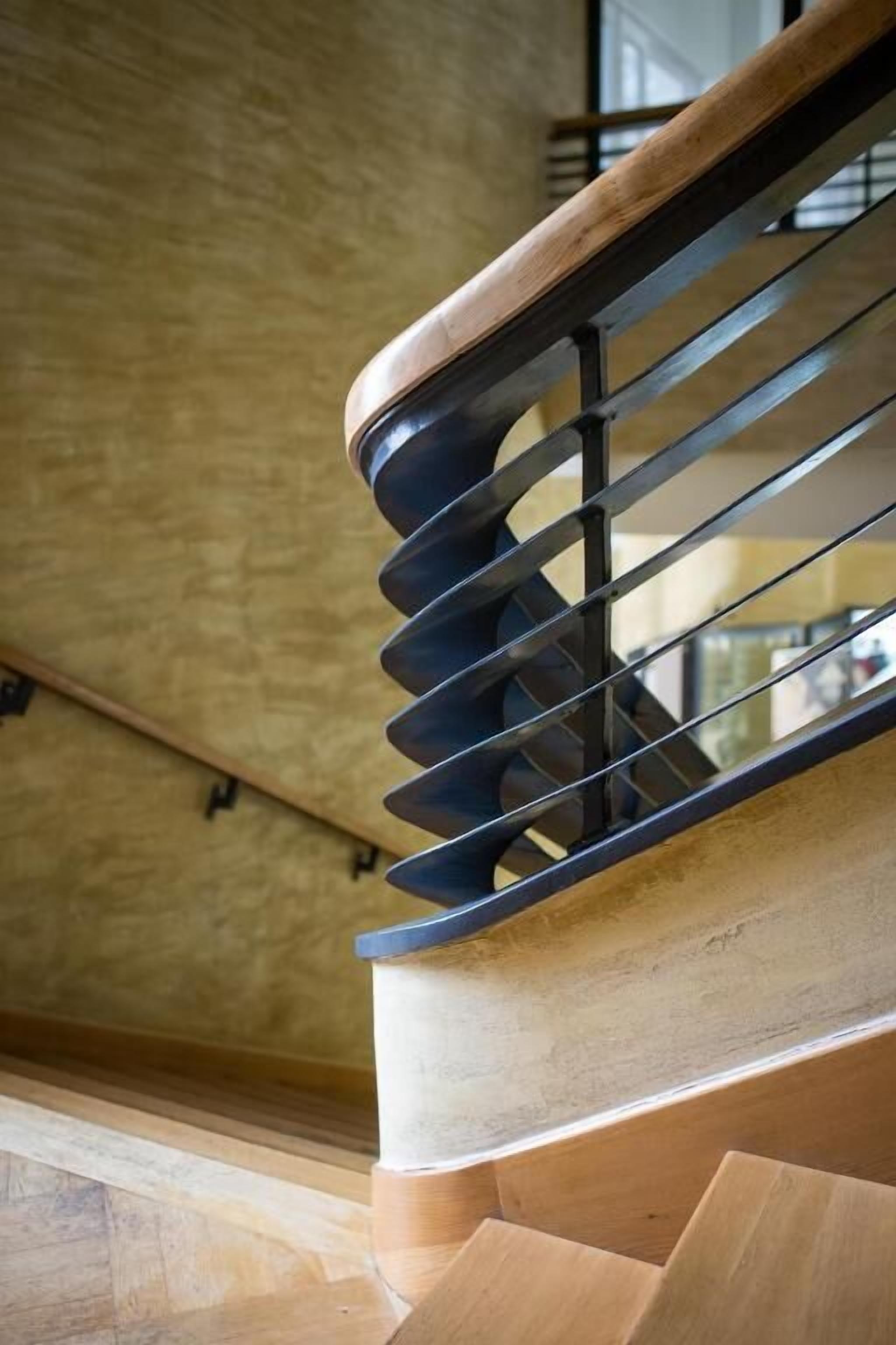 A wooden staircase with a metal handrail and a textured wall in the background.