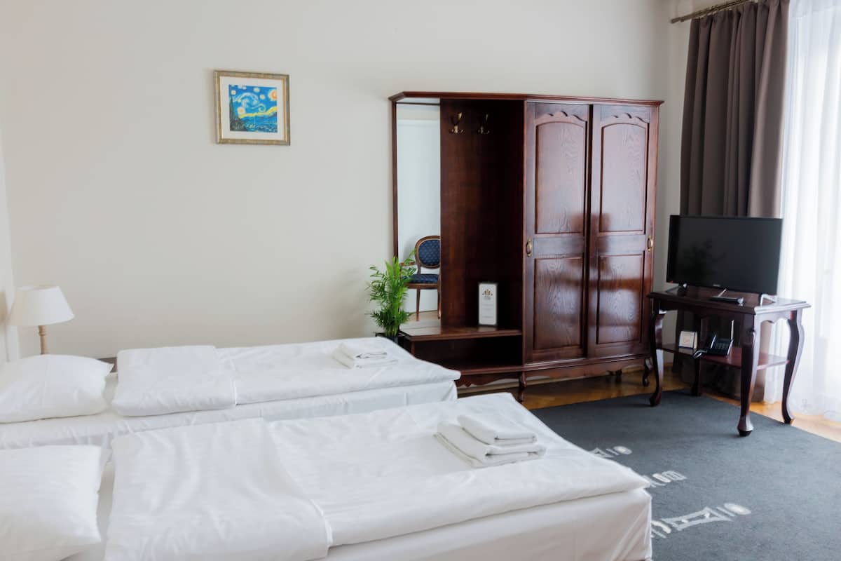 A hotel room with two beds, a wardrobe, a television, and a small table.