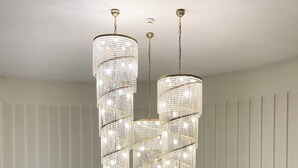 A modern interior with a large, ornate chandelier hanging from the ceiling, a white panel wall, and a small table with a potted plant. - Hotel Hutnik (Stalowa Wola)