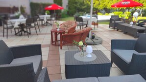 An outdoor patio area with wicker furniture, tables, and red umbrellas. - Hotel Hutnik (Stalowa Wola)