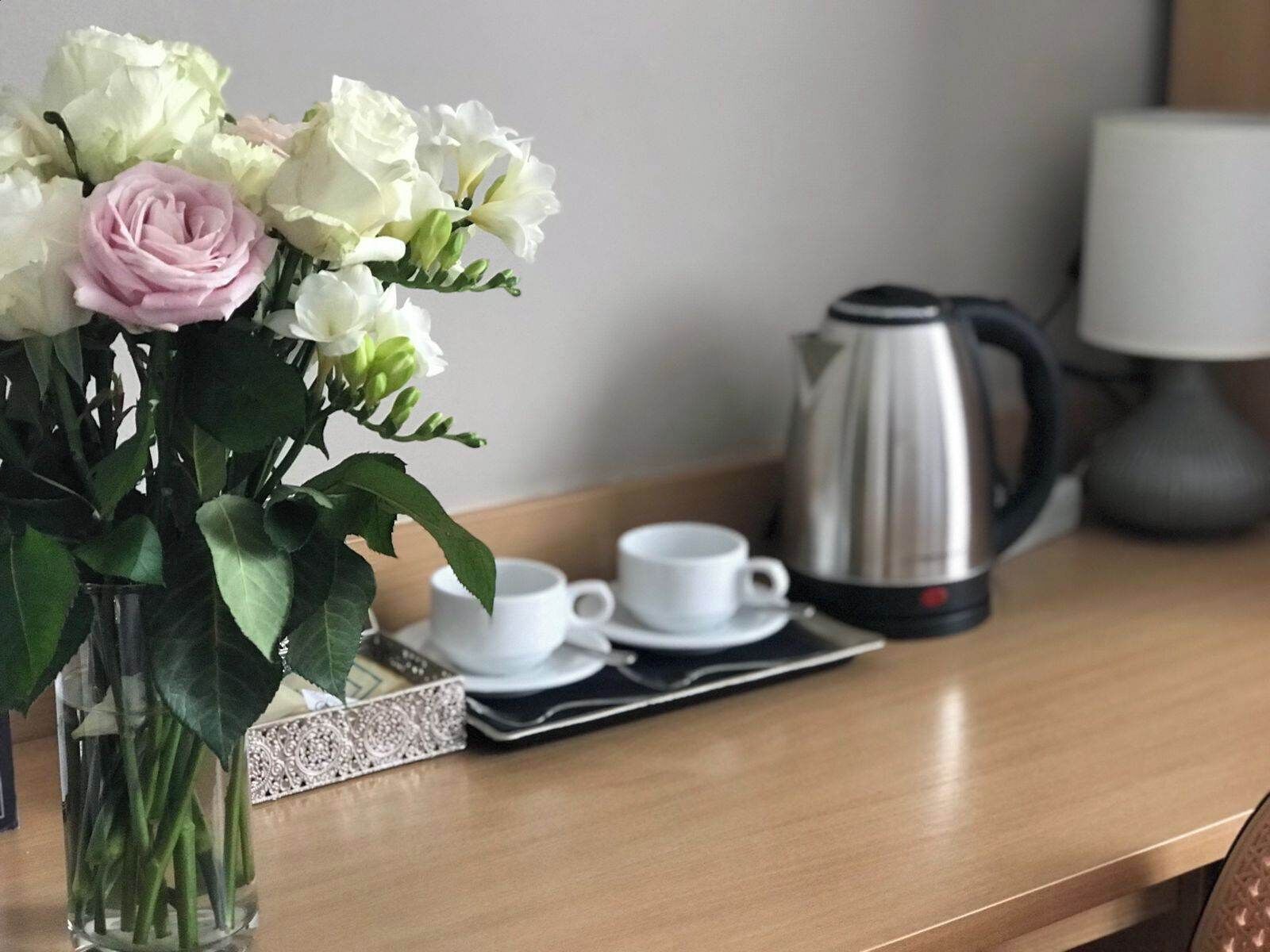 A wooden table with a coffee pot, two white cups, and a vase with flowers.