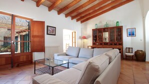 A living room with a sofa, a glass coffee table, wooden cabinets, and a large window. - Villa Martorell, 3 bedroom villa near crystalline beaches of Cala Sant Vicenç (Pollença)