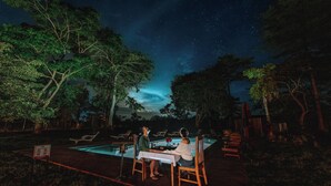 A couple dining at an outdoor poolside table under a starry sky.