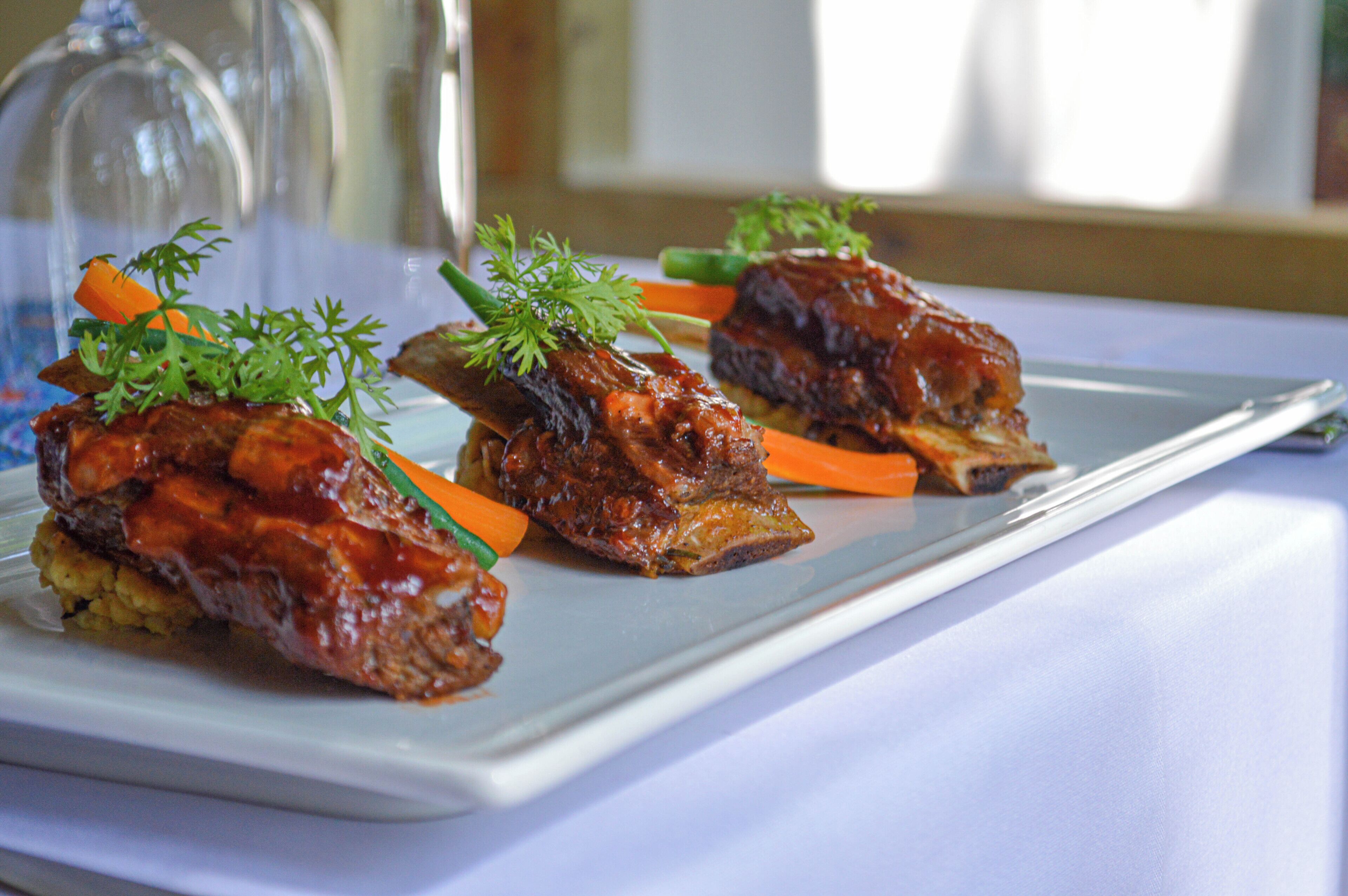 A white rectangular plate with three pieces of glazed meat garnished with parsley and carrot sticks.