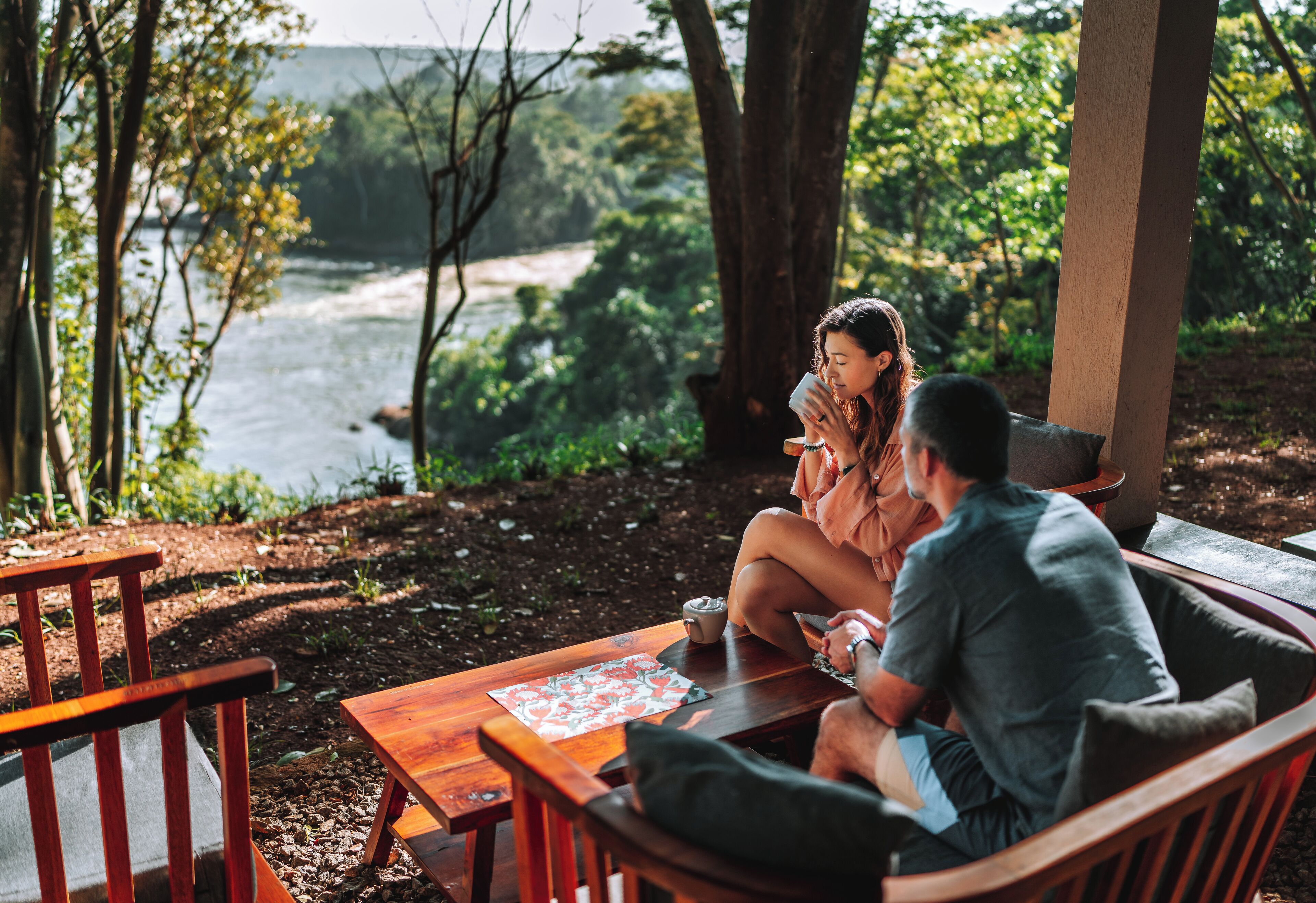 Une table et des chaises en bois, installées dans un espace extérieur ombragé, avec vue sur la rivière.