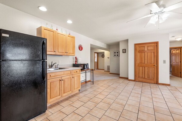A kitchen with a black refrigerator, wooden cabinets, a tiled floor, and a ceiling fan. - Bohemian Breeze: Oceanside | Pool and Hot Tub (Southern Shores)