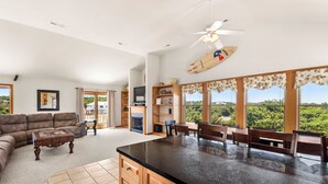 A spacious living room with a large sofa, a coffee table, and a kitchen area with a central island. - Bohemian Breeze: Oceanside | Pool and Hot Tub (Southern Shores)