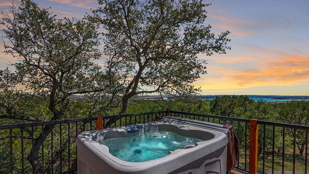 Ein Whirlpool auf einer Terrasse mit Blick auf Bäume und einen Sonnenuntergang.