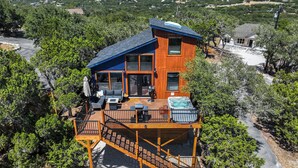 Eine zweistöckige Holzhütte mit einer Terrasse, Sitzgelegenheiten im Freien und einem Whirlpool.
