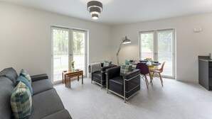 A modern living room with a sofa, a dining table with chairs, and a lamp. - Mhuilinn Apartment  -  an apartment that sleeps 3 guests  in 2 bedrooms (Stirling)