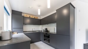 A modern kitchen with dark cabinetry, a central island, and built-in appliances. - Mhuilinn Apartment  -  an apartment that sleeps 3 guests  in 2 bedrooms (Stirling)