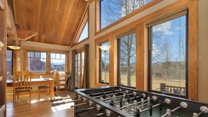 A spacious room with a foosball table, wooden furniture, large windows, and a view of the outdoors. - 701B Quail Family & pet friendly 3 bedroom rental private hot tub (Fraser)